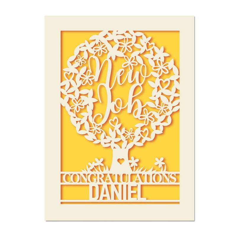 May include: A white paper card with a yellow background. The card features a cut-out design of a tree with the words "New Job" in the center. The text "Congratulations Daniel" is at the bottom of the card.