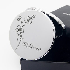 May include: A silver compact mirror with a floral design and the name Olivia engraved on the front.