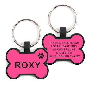 May include: Pink bone-shaped dog tag with black text and a paw print. The text reads "ROXY" on one side and "IF IAM OUT ALONE I AM LOST PLEASE FIND MY OWNER LUKE 07778553337 36 LONDON RD EX4 2EE" on the other side.