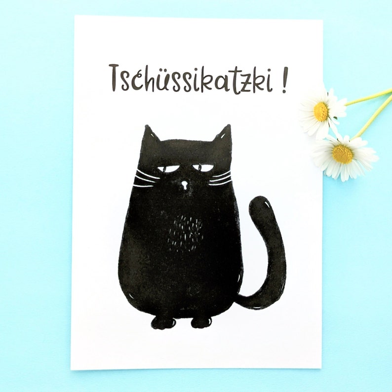 May include: A white card with the text "Tsch&uuml;ssikatzki!" above a black cat illustration. The cat has a grumpy expression, white whiskers, and a fluffy patch of fur on its chest. Daisies are in the upper right corner.