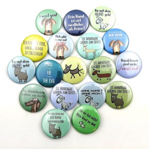 Könnte beinhalten: Eine Sammlung runder, farbenfroher Buttons zum Thema Hunde mit verschiedenen Illustrationen und Phrasen. Die Buttons zeigen Bilder verschiedener Hunderassen und Texte wie "I woof you!" und "You & Me & The Dog".
