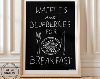 May include: A framed print with a black background and white text that reads "WAFFLES AND BLUEBERRIES FOR BREAKFAST." The image includes a fork, knife, and a plate with waffles and blueberries. The frame is a light wood color.