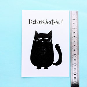 May include: A black and white illustration of a grumpy cat with the text "Tsch&uuml;ssikatzki!". The cat is drawn in a simple, cartoon style. A ruler is placed next to the illustration, measuring up to 16 cm.