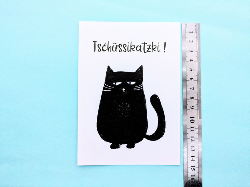 May include: A black and white illustration of a grumpy cat with the text "Tsch&uuml;ssikatzki!". The cat is drawn in a simple, cartoon style. A ruler is placed next to the illustration, measuring up to 16 cm.