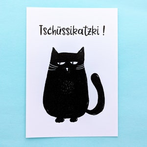 May include: A white card with a black illustration of a grumpy cat. The cat has a round body, a curved tail, and white whiskers. The text "Tsch&uuml;ssikatzki!" is printed above the cat in black.