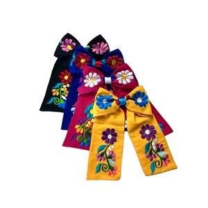 May include: Four embroidered fabric bows in different colors, including black, blue, red, and yellow. Each bow features a floral design with colorful flowers and leaves.