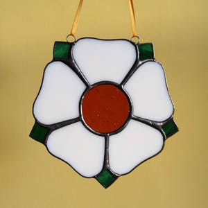 May include: A stained glass window hanging ornament featuring a white flower with a red center and green accents.