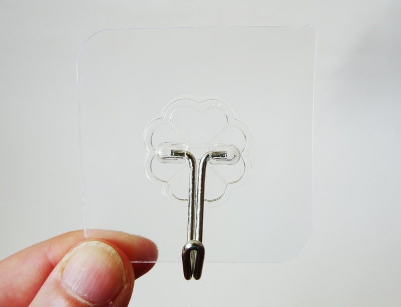 May include: A clear plastic adhesive hook with a silver metal hook. The hook is designed to be attached to a smooth surface.