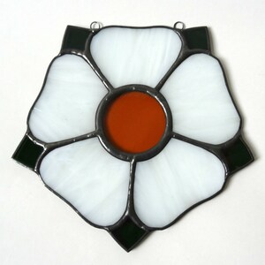 May include: A stained glass window depicting a white flower with a dark green border and an orange center.