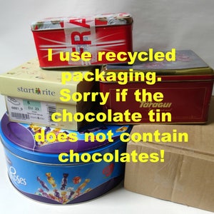 May include: A stack of four empty tin boxes, including a red box with the text "FRA", a yellow box with the text "start rite", a red box with the text "Taragui", and a blue box with the text "Roses". The text "I use recycled packaging. Sorry if the chocolate tin does not contain chocolates!" is written in yellow on the boxes.