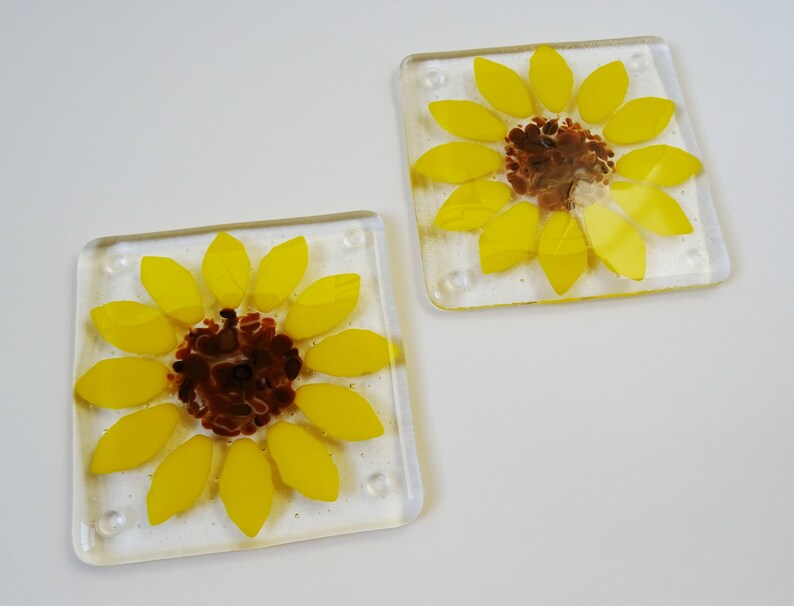 Peut inclure: Deux sous-verres en verre avec un motif de tournesol. Les tournesols sont jaunes avec des centres bruns et sont plac&eacute;s sur un fond de verre transparent.