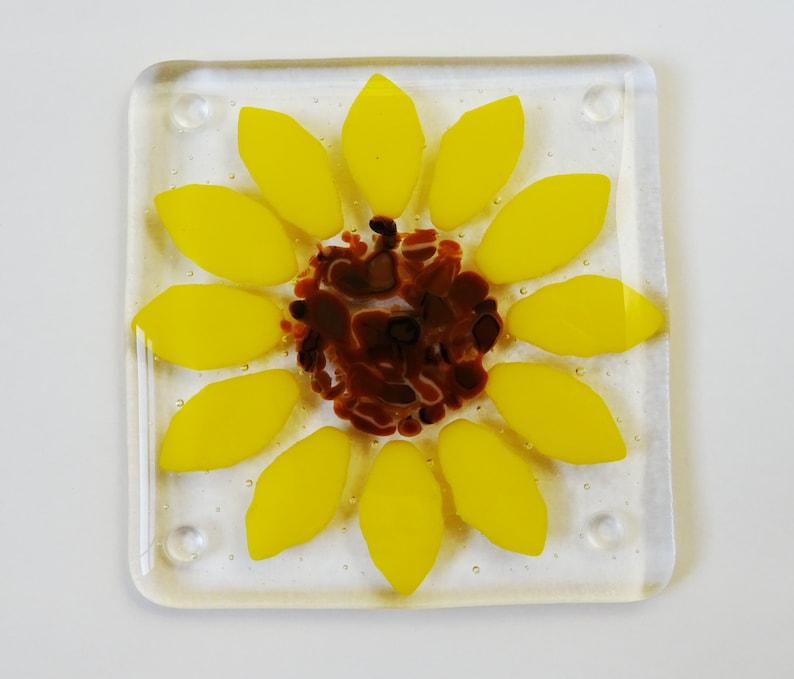 Peut inclure: Un dessous de verre en verre avec un motif de tournesol. Le tournesol est jaune avec un centre brun. Le dessous de verre est en verre transparent.