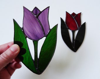 May include: Two stained glass tulips, one purple and one red, with black outlines and green leaves.