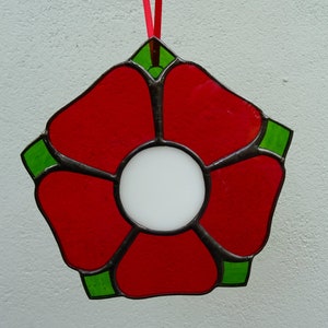 May include: A red stained glass flower with a white center and green accents. The flower is hanging from a red ribbon.
