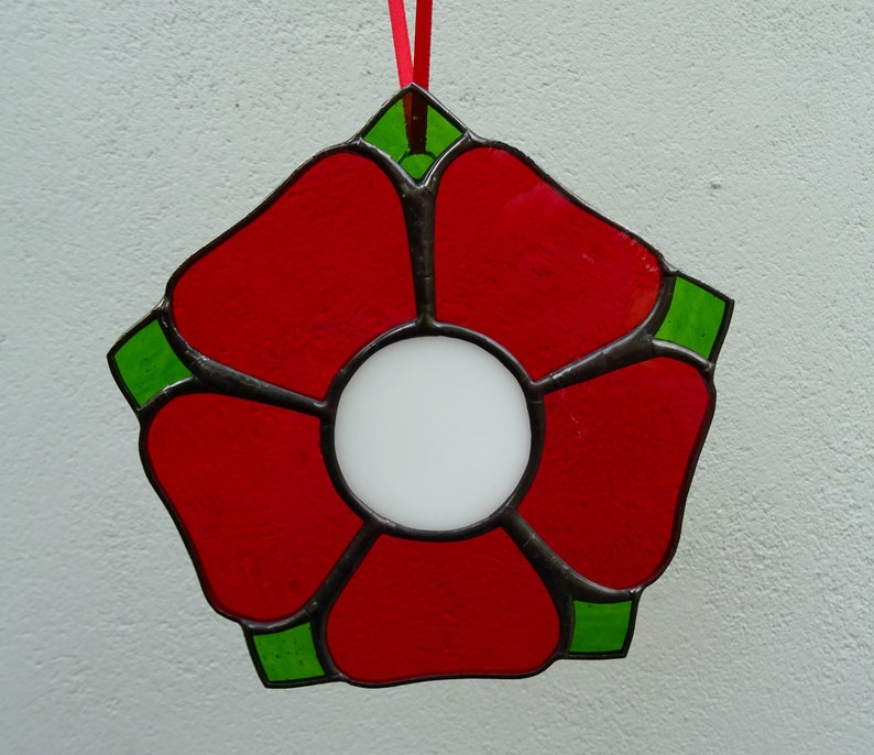 May include: A red stained glass flower with a white center and green accents. The flower is hanging from a red ribbon.