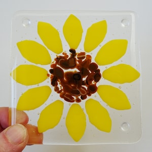 Peut inclure: Un dessous de verre en verre avec un motif de tournesol. Le tournesol est jaune avec un centre brun. Le dessous de verre est transparent et de forme carr&eacute;e.