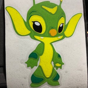 Könnte beinhalten: Ein grüner und gelber Comic-Alien mit großen Augen und einem kleinen Mund. Das Alien hat zwei Antennen auf dem Kopf und steht auf einem weißen Hintergrund.
