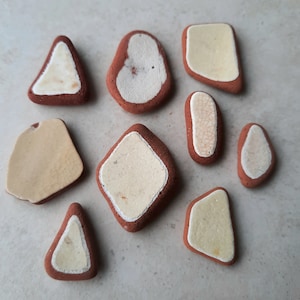May include: Assortment of nine small, irregularly shaped ceramic tiles with a white glaze and brown edges. The tiles have a variety of shapes, including triangles, squares, and rectangles.