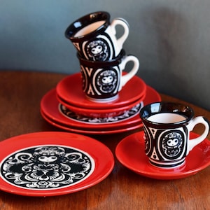 以下が含まれることがあります： 赤と黒のセラミックティーカップとソーサーのセット。カップとプレートは白黒のデザインです。カップは積み重ねられ、ソーサーは積み重ねて配置され、個別に配置されています。