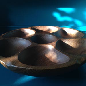 Puede incluir: Un bol de servir de madera con seis compartimentos individuales. El bol es de color marrón oscuro y tiene un acabado liso y pulido.