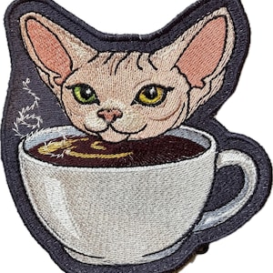 May include: Embroidered patch featuring a Sphynx cat's head emerging from a coffee cup. The cat has green and yellow eyes, and the cup contains dark brown liquid. The patch has a dark blue border and white steam detail.