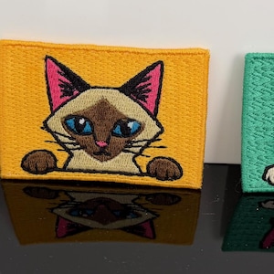 May include: Three rectangular embroidered patches featuring cat illustrations. The left patch is light blue with a black and white cat, the center is yellow with a Siamese cat, and the right is mint green with a calico cat, all with paws visible.