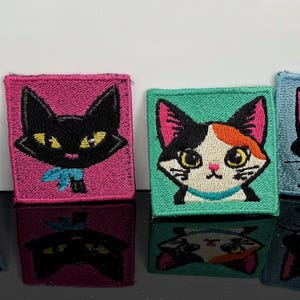 May include: A set of six square fabric patches, each featuring a unique embroidered cat portrait. The cats are set against vibrant backgrounds of blue, light blue, pink, teal, and yellow, showcasing various feline breeds and expressions.