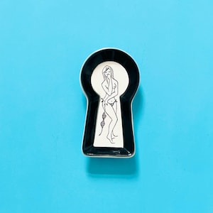 May include: A keyhole-shaped ceramic trinket dish featuring a black border and a white centre. The centre displays a black line art illustration of a standing figure wearing a two-piece swimsuit, with a DNA strand graphic positioned near the legs.