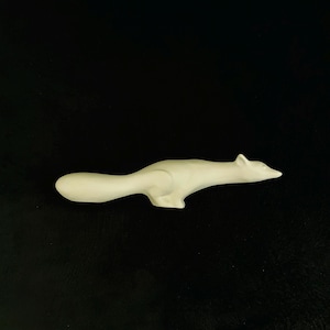 May include: A cream-coloured ceramic fox figurine, in a sleek, minimalist style. The fox is in a running pose, with its body elongated and its tail curved. The figurine is set against a black background.