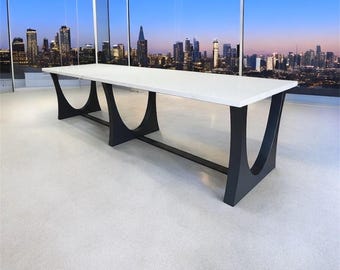 May include: A long, rectangular table with a white top and black, curved legs. The table is approximately 10 feet long and is set against a backdrop of a cityscape at dusk. The legs are made of a dark, matte material.