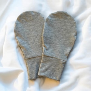 May include: A pair of gray cotton mitten-style hand covers. The covers are made of a soft, stretchy fabric and have a simple design.