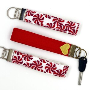 May include: Three key fobs with metal hardware. Two are white with a red and burgundy pinwheel pattern. The third is solid red with a gold heart and a key attached.