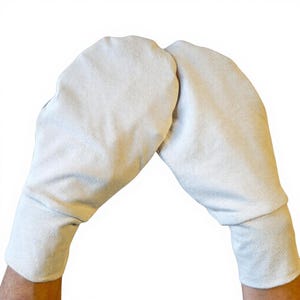 Può includere: Un paio di guanti color bianco sporco, in materiale simile alla pelle scamosciata. I guanti hanno una forma arrotondata e un polsino al polso. Lo sfondo è bianco.
