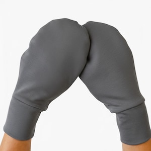 Puede incluir: Un par de manoplas de color gris oscuro sólido con una construcción de tela lisa y sencilla, forma redondeada en la parte superior y un puño ancho y ajustado en la base. Las manoplas presentan un diseño simple y un acabado mate uniforme.