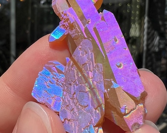 May include: A cluster of iridescent crystals with a vibrant display of colors, including purple, blue, and gold. The crystals have a rough, textured surface and are held in a hand. The crystals are a natural, decorative item.