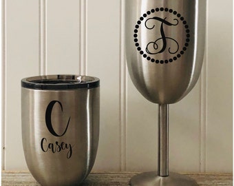 Puede incluir: Dos vasos de acero inoxidable con tapas negras. El vaso de la izquierda tiene una letra negra "C" y el nombre "Casey" impreso en él. El vaso de la derecha tiene una letra negra "T" dentro de un círculo con puntos negros alrededor.