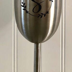 May include: A stainless steel wine tumbler with a black vinyl decal of a wreath with the letter "S" in the center.