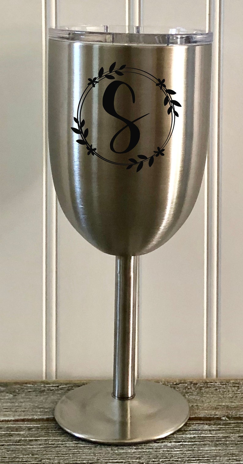 May include: A stainless steel wine tumbler with a black vinyl decal of a wreath with the letter "S" in the center.