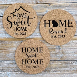 May include: Three cork coasters with black text. The first coaster says "HOME Sweet HOME Est. 2023". The second coaster says "HOME Resnick Est. 2023" with a silhouette of the state of Georgia. The third coaster says "HOME Sweet HOME Est. 2023".