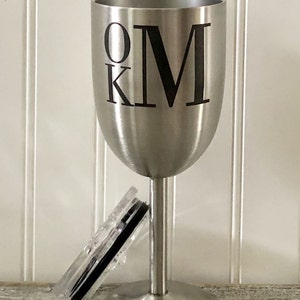 May include: A stainless steel wine tumbler with a black lid and the initials "OKM" printed on the side.