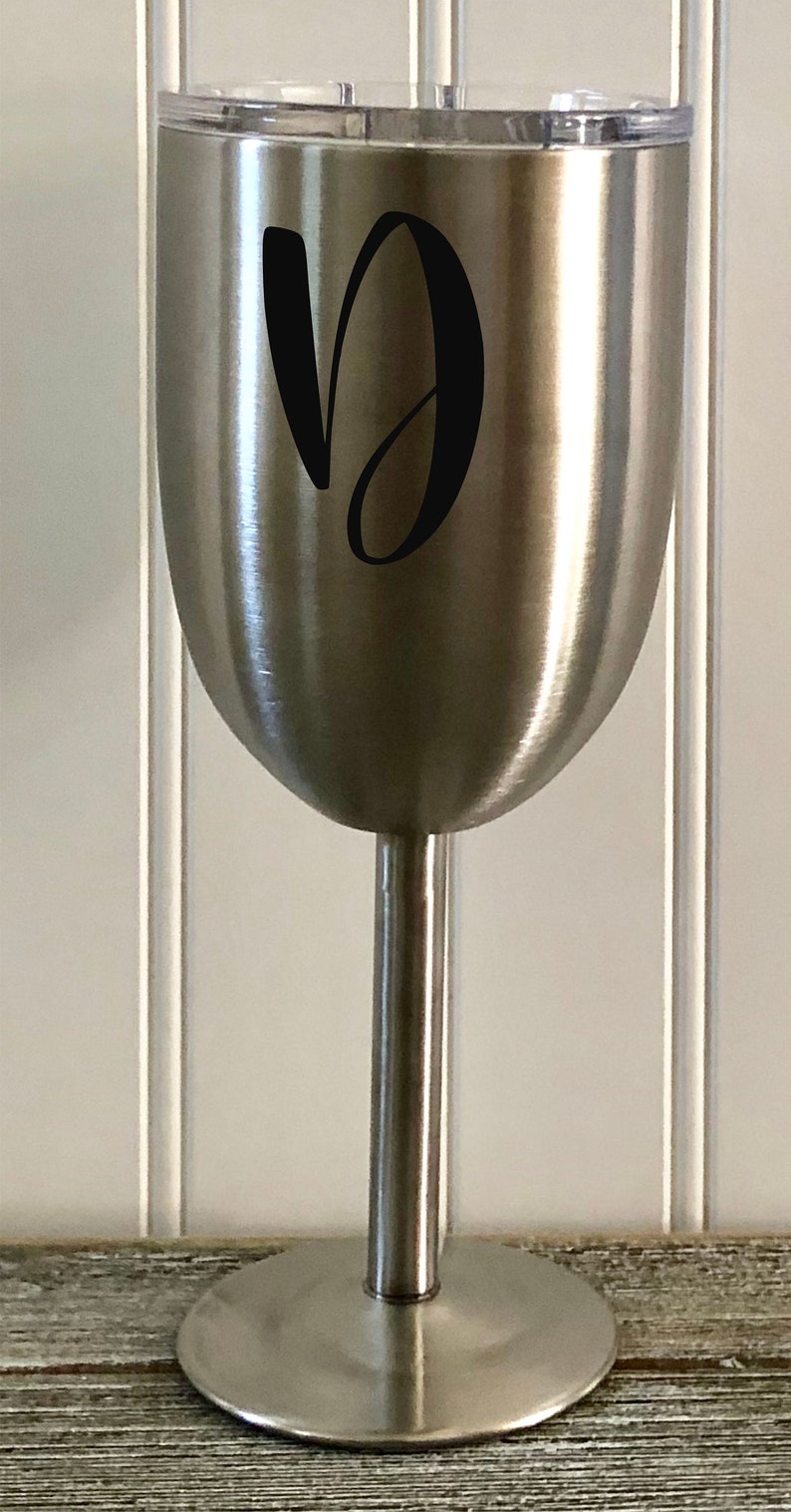 May include: A stainless steel wine tumbler with a black letter "D" on the side. The tumbler has a lid and a stem.
