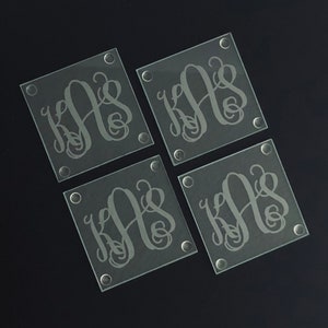 May include: Set of four glass coasters with a monogram design. Each coaster features the letters "KAS" in a cursive script.