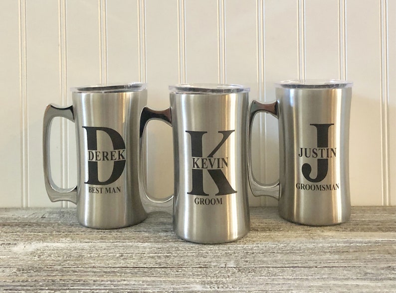 Puede incluir: Tres tazas de viaje de acero inoxidable con tapas. Las tazas est&aacute;n personalizadas con los nombres Derek, Kevin y Justin, junto con sus roles en una fiesta de boda: padrino, novio y padrino.