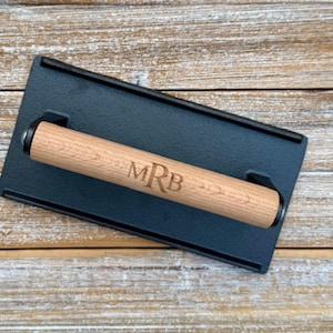 May include: A black cast iron grill press with a wooden handle. The handle is engraved with the initials "MRB".