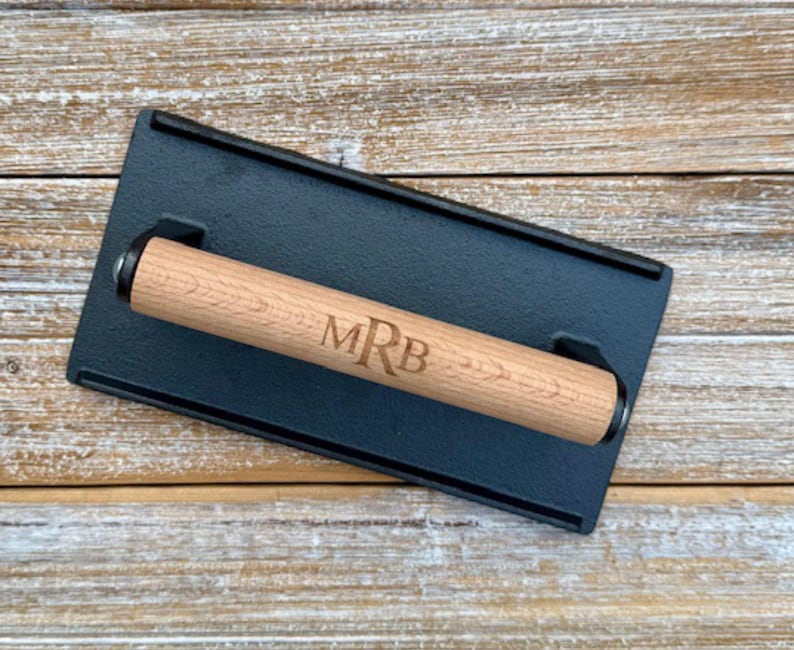 May include: A black cast iron grill press with a wooden handle. The handle is engraved with the initials "MRB".