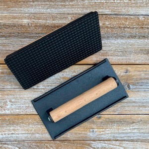 May include: A black cast iron grill press with a wooden handle. The press has a textured surface for creating grill marks on food.