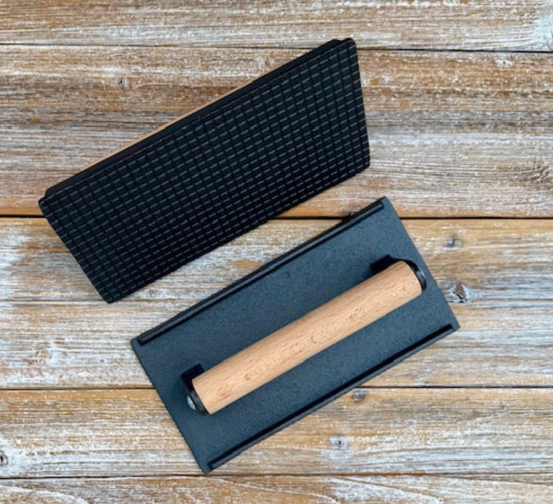 May include: A black cast iron grill press with a wooden handle. The press has a textured surface for creating grill marks on food.