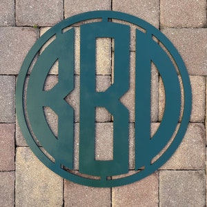 Puede incluir: Un letrero de pared circular de color verde oscuro que presenta las letras B, R y D en un formato de monograma estilizado. Las letras están interconectadas dentro de un marco circular sólido, creando un diseño coherente y limpio.