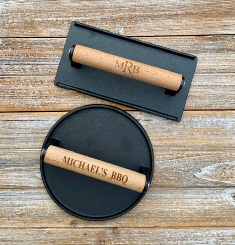 May include: Two cast iron burger press with wooden handles. The top press has the initials "MRB" engraved on the handle. The bottom press has the text "MICHAEL'S BBQ" engraved on the handle.