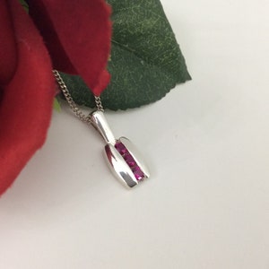 May include: A silver pendant necklace with a rectangular design featuring three pink gemstones.